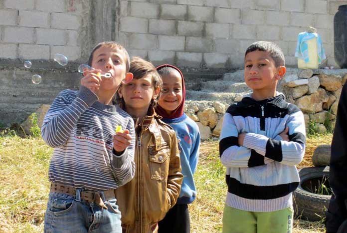 A group of young Palestinian children blowing bubbles and smiling.