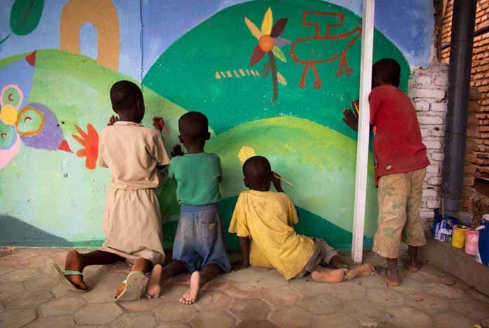 A small group of Burundian children painting a mural on a wall.