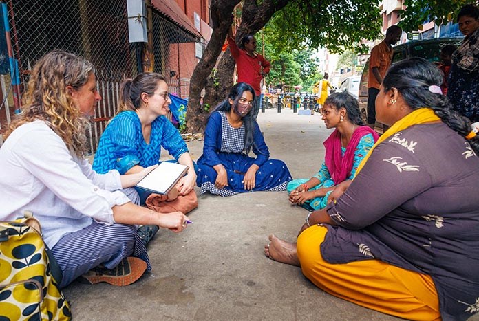 Two women from the UK interview young women from India on the pavement.