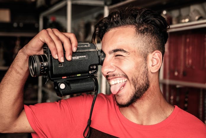 A young Palestinian man looks through an old Super8 movie camera while pulling a funny face.