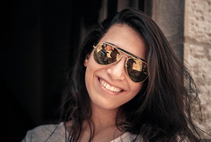 A young Palestinian women wearing sunglasses smiles for the camera.