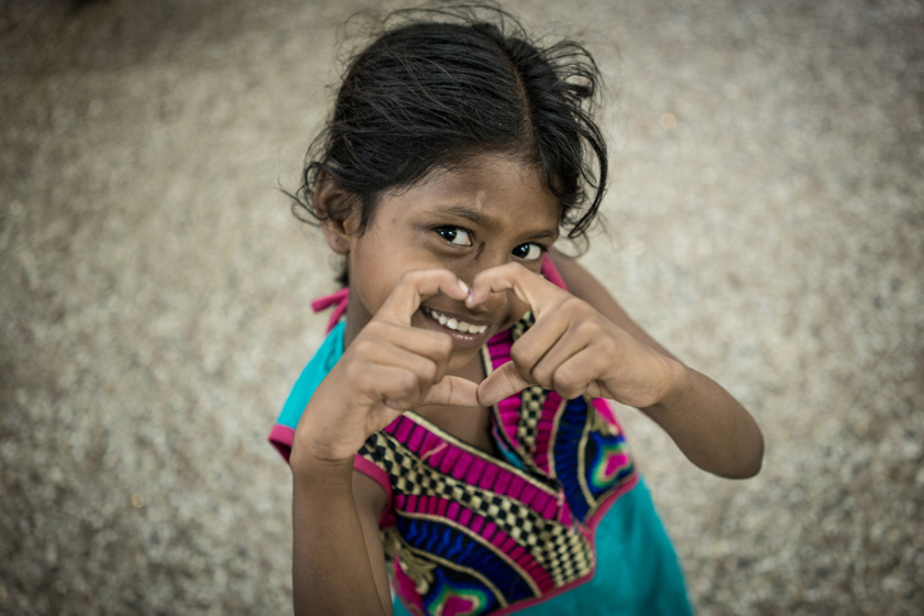 A young Indian girl makes the shape of a love heart with her hands while smiling.