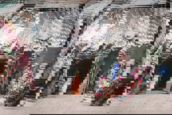 An elderly Indian lady sits on the pavement outside her so-called house.