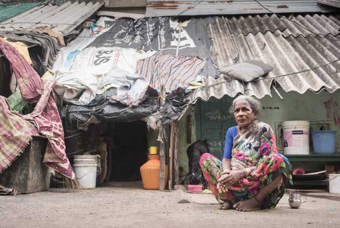 An elderly Indian lady sits on the pavement outside her so-called house.