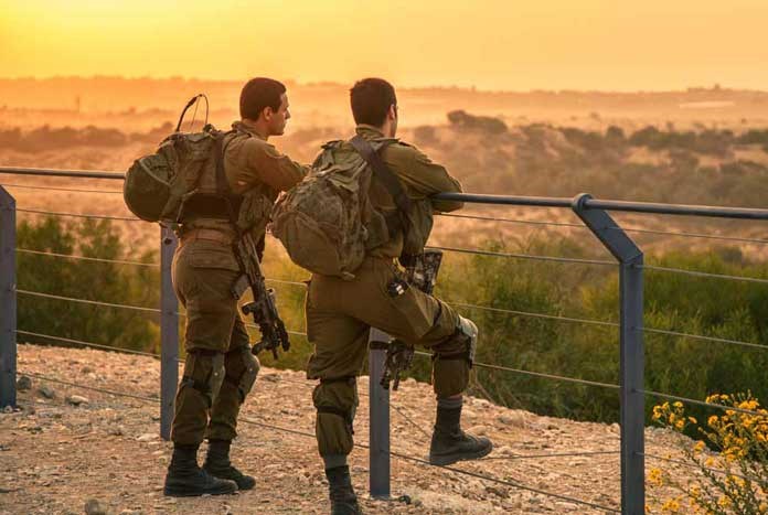 Two Israeli soldiers looking out over the Gaza Strip at sunset.