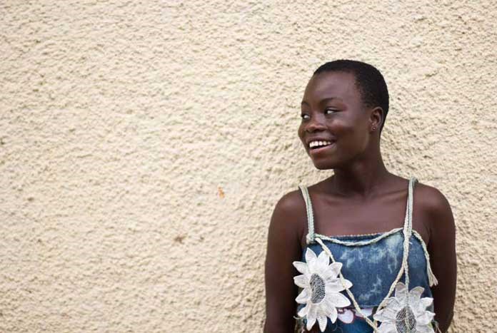 A young Burundian women standing in front of a wall and smiling.