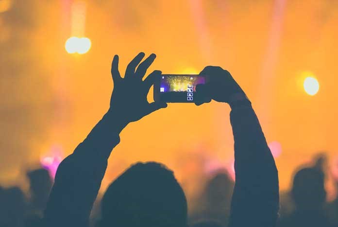 A young person filming a pop concert on their mobile phone.
