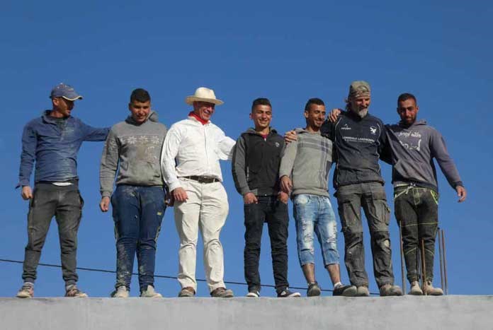 Palestinian builders and volunteers from the UK standing on top of a rebuilt home in the West Bank.