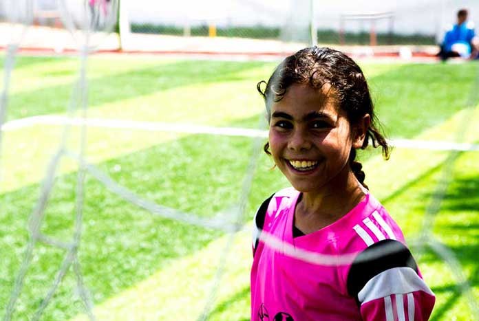 A young girl in Gaza playing football and smiling.