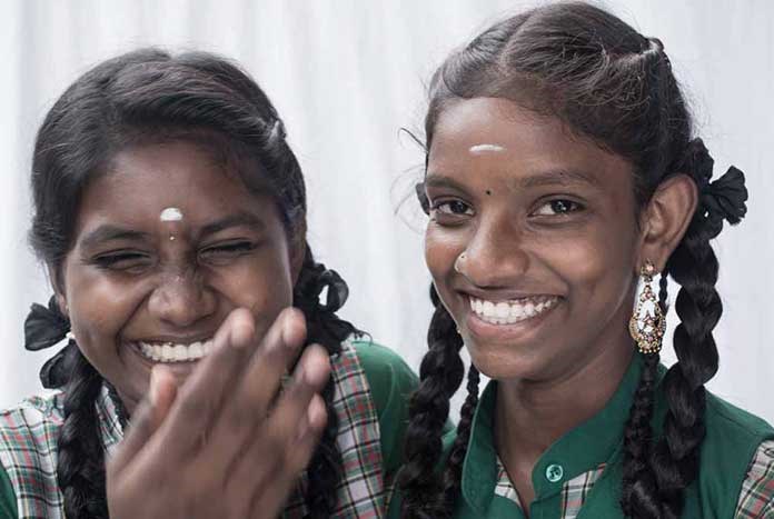 Two Indian girls dressed in school uniforms laugh for the camera.