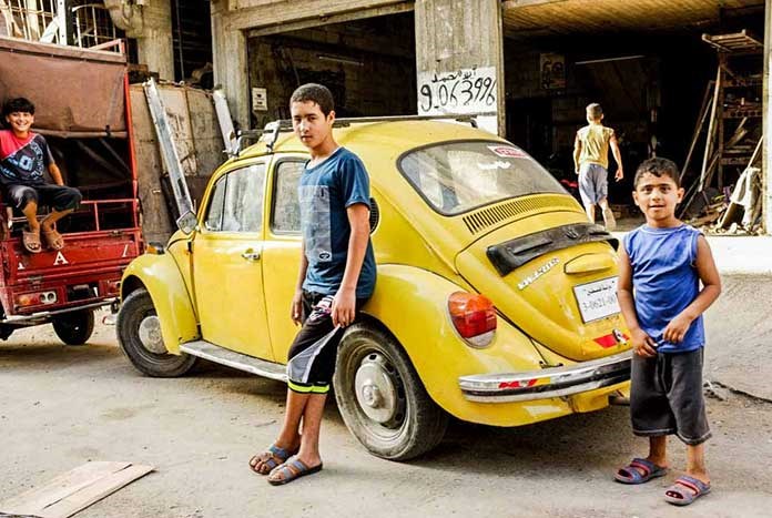 Two boys standing in front of a yellow VW Beetle in a market in Gaza City.