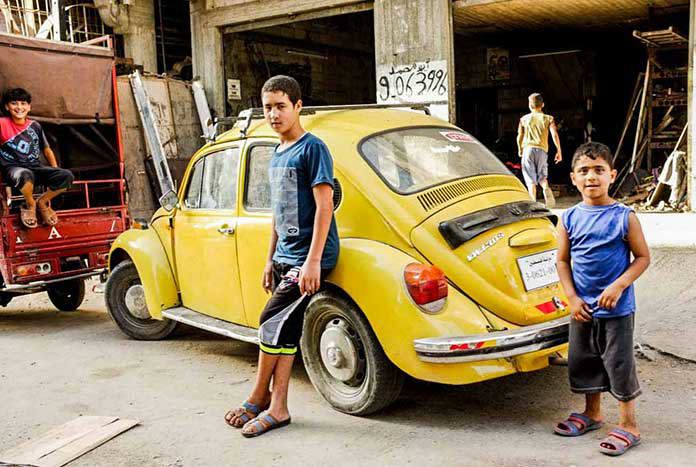 Two boys standing in front of a yellow VW Beetle in a market in Gaza City.