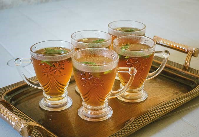 A tray of five ornate glass cups containing mint tea.
