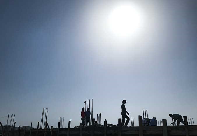Builders in silhouette on the roof of a house they are rebuilding in Palestine against a bright blue sky.