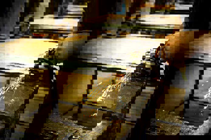 An angle-grinder being used on a piece of metal in a vice with sparks flying.