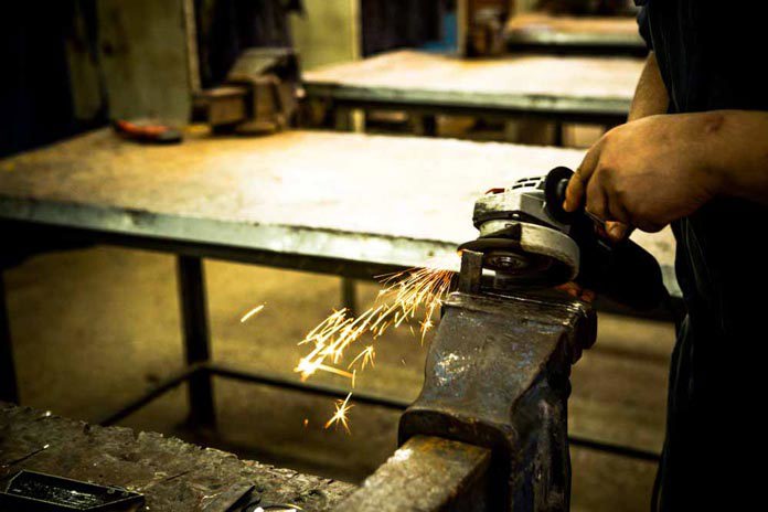 An angle-grinder being used on a piece of metal in a vice with sparks flying.