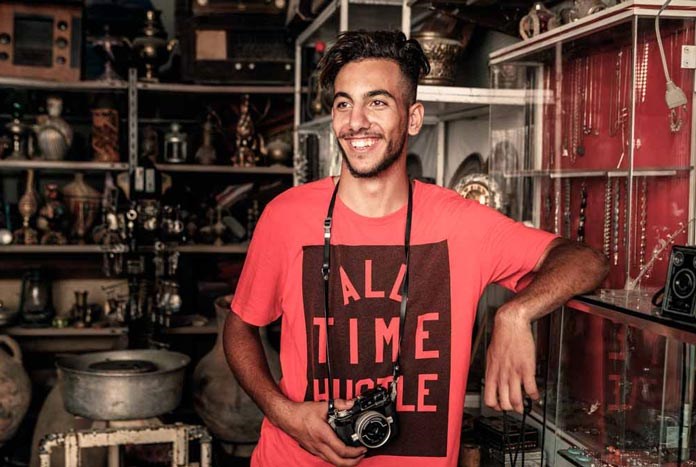 A young man smiles as he wears his camera around his neck.