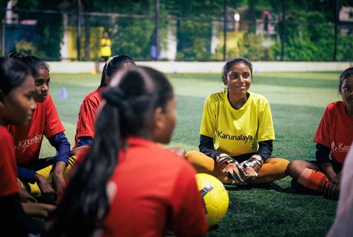 Young Indian women in their football kits sitting on the ground smiling.