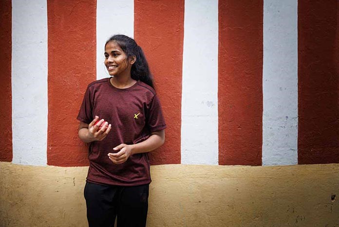 Monisha, 17 from Chennai, India, smiling as she plays with a cricket ball.