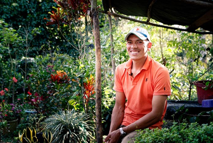 A Nicaraguan man sits in his garden outside his house smiling.