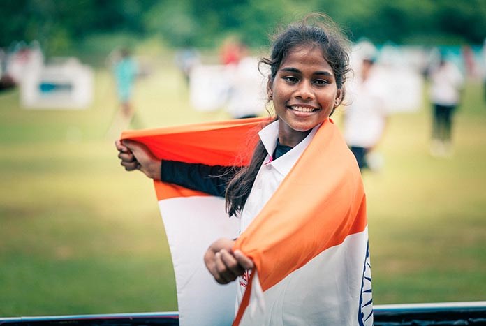 A young Indian women wraps herself in the Indian flag and smiles.