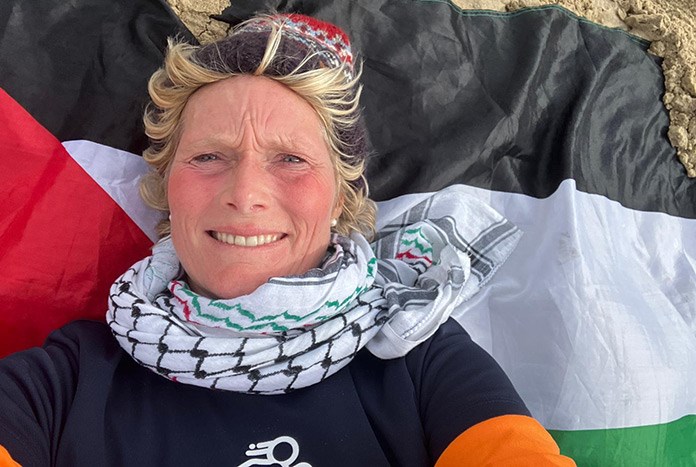 A woman laying on a Palestinian flag on a beach wearing a keffiyeh scarf.