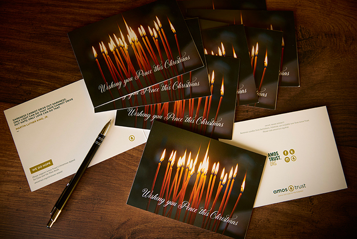 Christmas cards featuring lit candles laying on a wooden table with a pen.