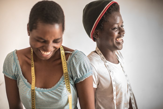 Two young Tanzanian women laughing together with tape measures around their necks.