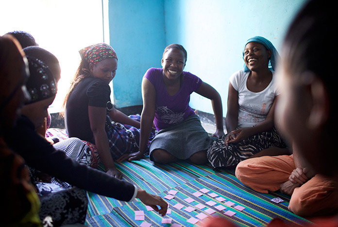 A small group of Tanzanian women sitting on the floor smiling and laughing.