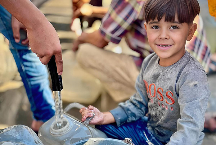 A young smiles for the camera as he collects fresh water in Gaza.